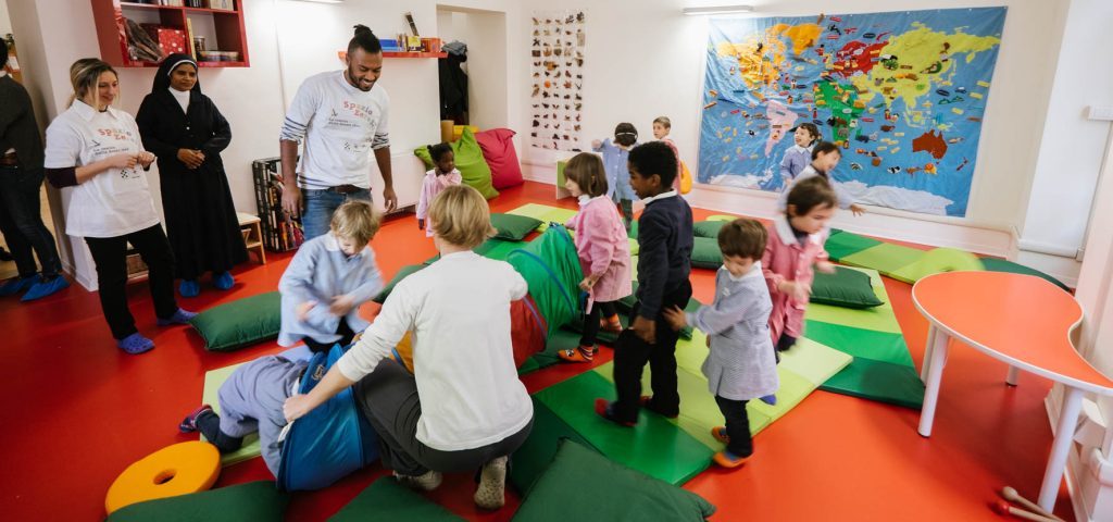 Alcuni bambini giocano con il tunnel da gioco e con gli insegnanti nella stanza di Spazio ZeroSei con il pavimento rosso