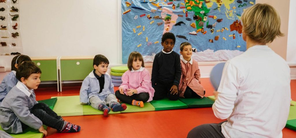 Alcuni bambini e un'insegnante seduti a terra su materassini verdi nella stanza di Spazio ZeroSei con il pavimento rosso