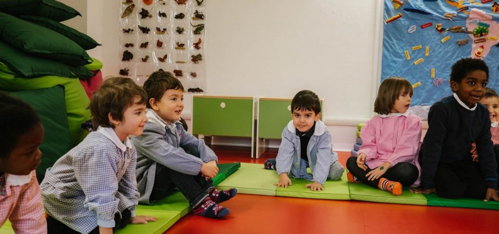 Alcuni bambini seduti a terra su materassini verdi nella stanza di Spazio ZeroSei con il pavimento rosso