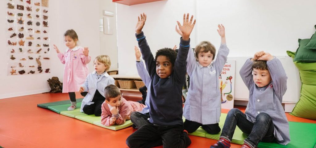 Un gruppo di bambini nella stanza col pavimento rosso di Spazio ZeroSei sta alzando le braccia