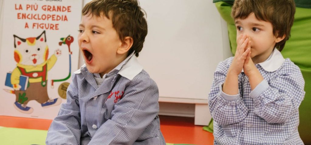 Due bambini seduti a terra, uno di questi sta sbadigliando