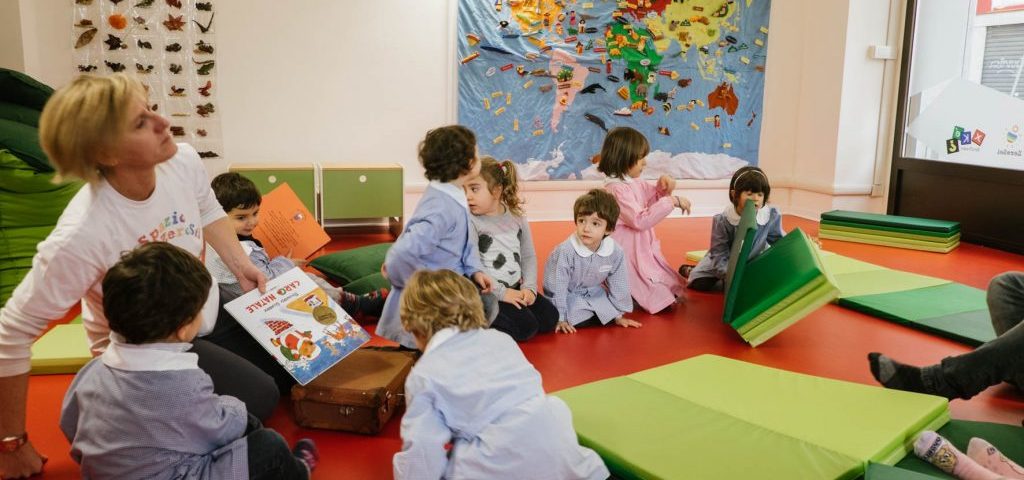 Un'insegnante sta leggendo un libro a un gruppo di bambini seduti a terra nella stanza di Spazio ZeroSei con il pavimento rosso