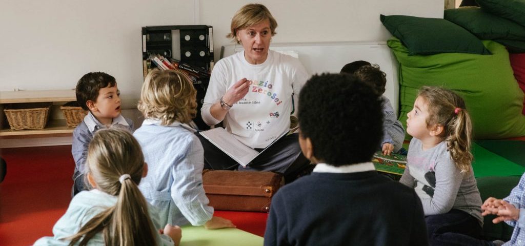 Un'insegnante sta leggendo un libro a un gruppo di bambini seduti a terra nella stanza di Spazio ZeroSei con il pavimento rosso