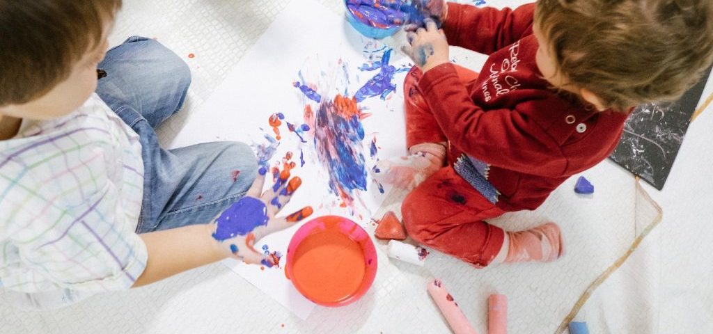 Due bambini visti dall'alto dipingono con le mani un grosso foglio bianco