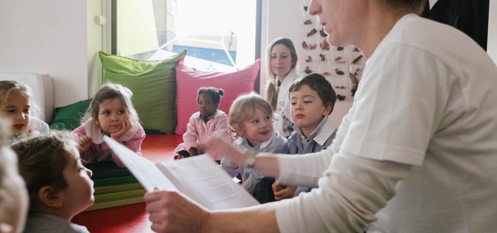 Un'insegnante sta leggendo un libro a un gruppo di bambini seduti a terra nella stanza di Spazio ZeroSei con il pavimento rosso