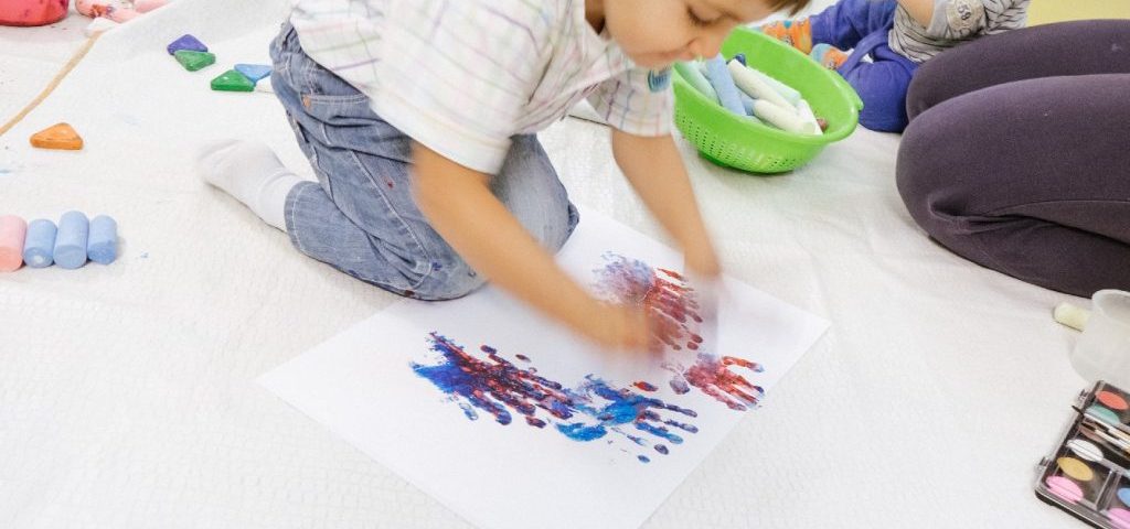Un bambino dipinge un grosso foglio bianco lasciando le impronte delle sue mani