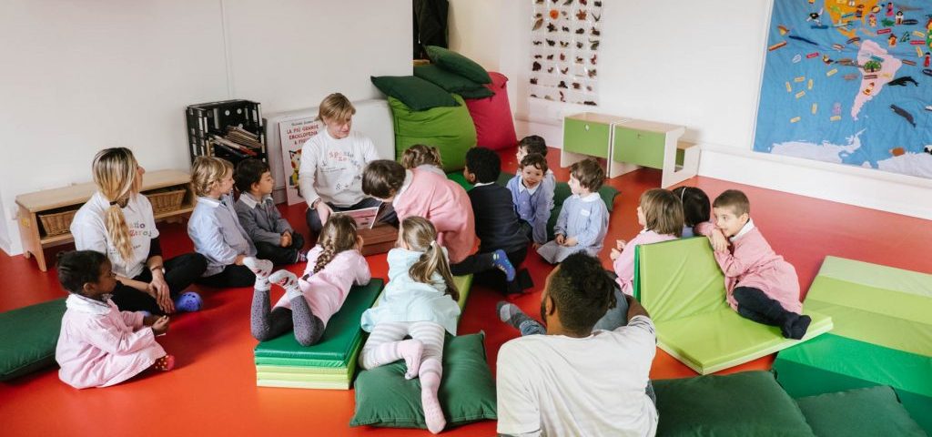 Un'insegnante sta leggendo un libro a un gruppo di bambini seduti a terra nella stanza di Spazio ZeroSei con il pavimento rosso