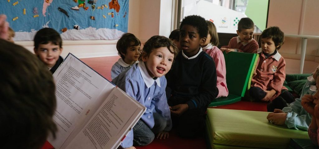 Un'insegnante sta leggendo un libro a un gruppo di bambini seduti a terra nella stanza di Spazio ZeroSei con il pavimento rosso