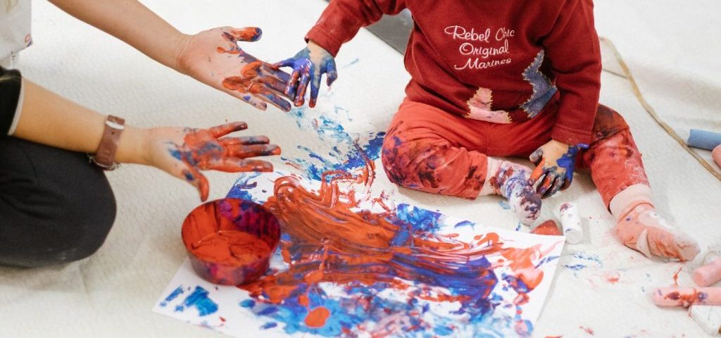 Un bambino aiutato da un'insegnante dipinge con le mani un grosso foglio bianco