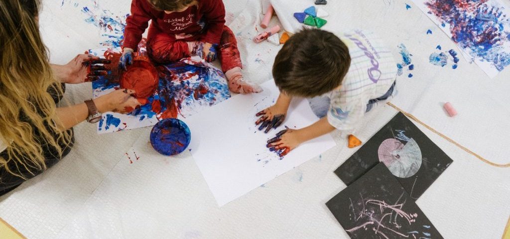 Dei bambini stanno dipingendo con le loro impronte delle mani dei grossi fogli bianchi