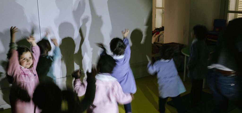 Un gruppo di bambini in una stanza semibuia gioca a proiettare le ombre su una parete bianca