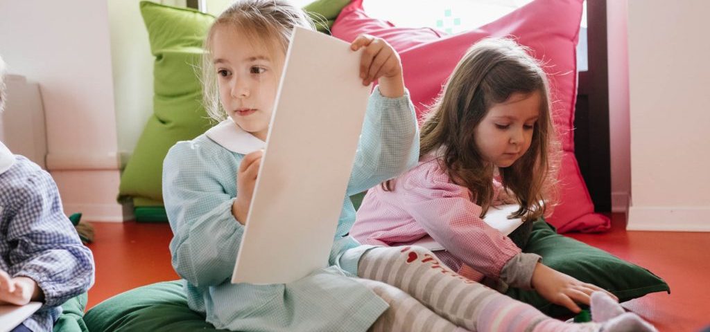 Due bambine sedute su grossi cuscini verdi. Una sta disegnando su un foglio bianco