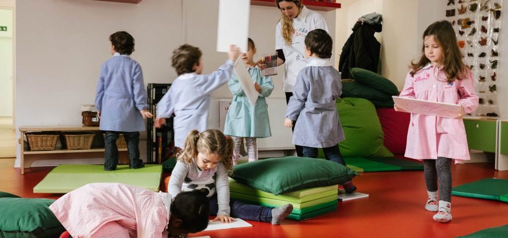 Un gruppo di bambini con un'insegnante in una stanza di Spazio ZeroSei. A terra vi sono cuscini e materassi colorati