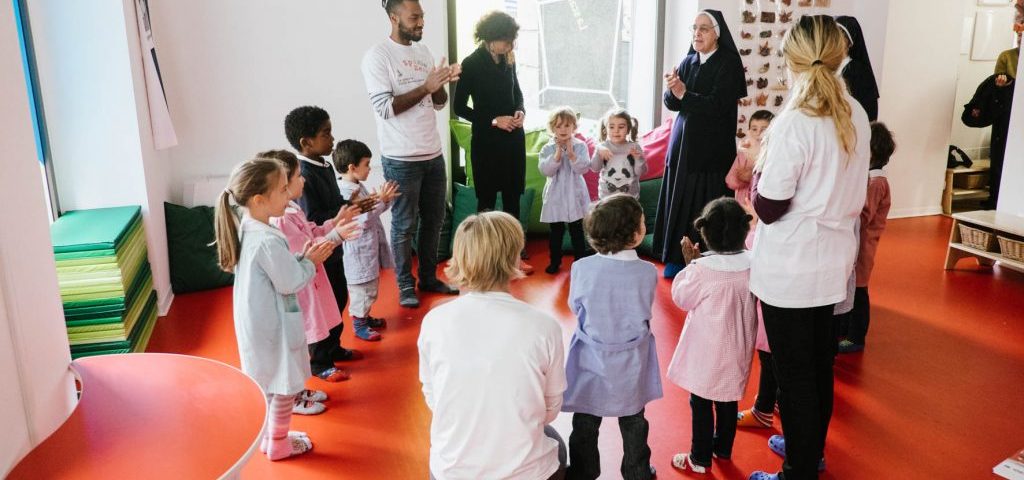 Un gruppo di bambini in cerchio con gli insegnanti e due suore