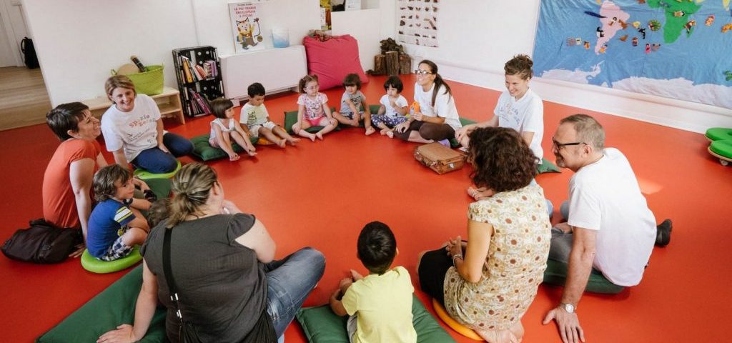 Bambini, insegnanti e genitori seduti in cerchio nella sala di ingresso a Spazio ZeroSei